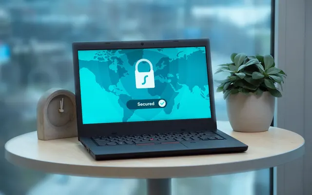 Un ordinateur portable affiche une icône de cadenas sur une table, à côté d'une plante et d'une horloge