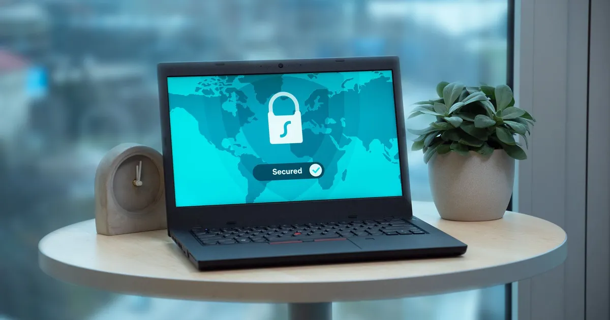 Un ordinateur portable affiche une icône de cadenas sur une table, à côté d'une plante et d'une horloge